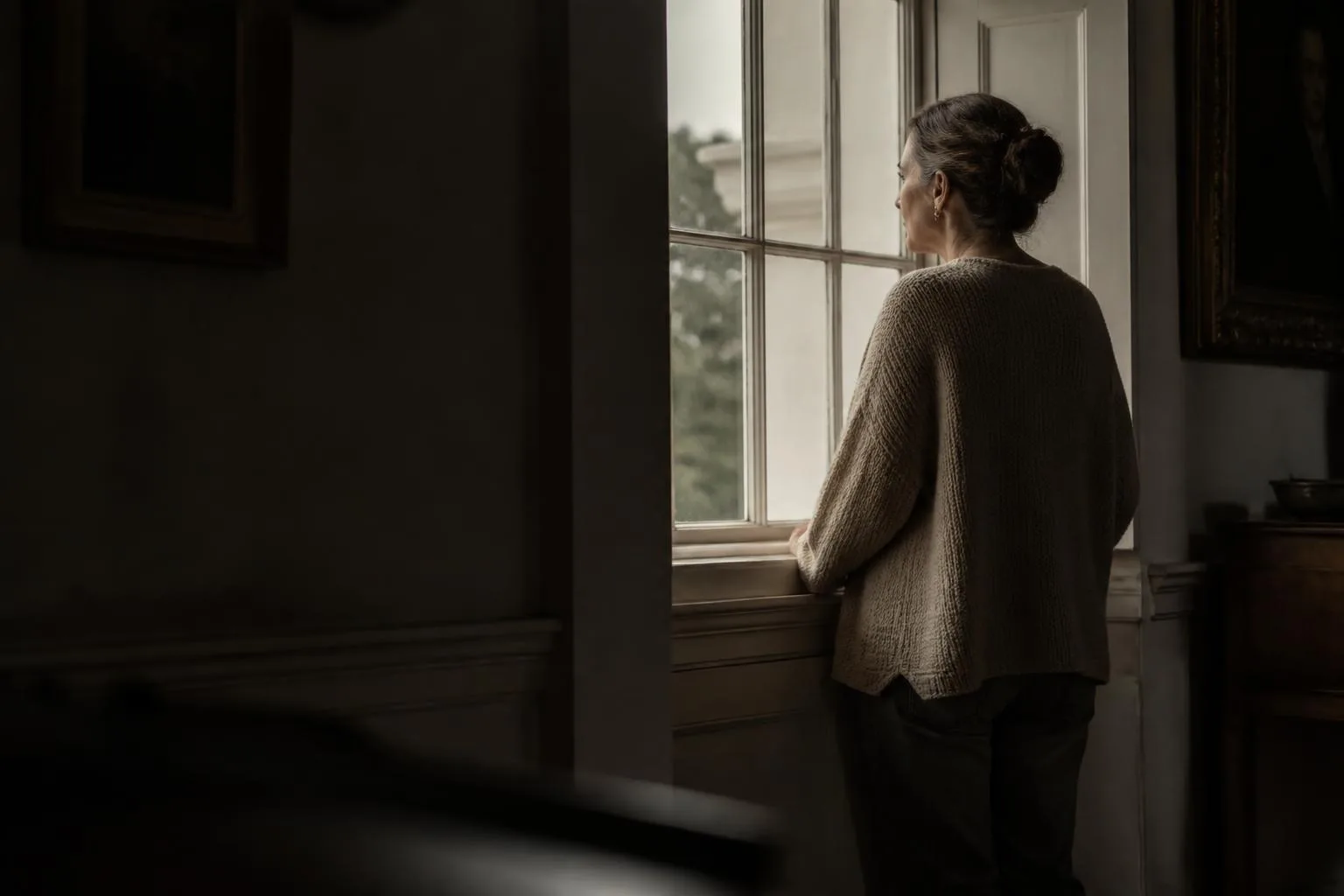 A woman at a tall Georgian sash window, face just catching the late light.